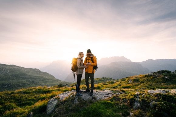 Two hikers on a mountain top looking at a compass at sunset