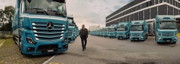 A woman sits outside at a wooden table in the evening sun and is researching early retirement on her laptop.