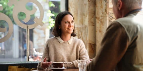 A smiling woman in a cafe talking to a colleague